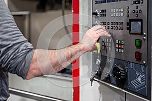 Worker pressing buttons on CNC machine control board in factory.