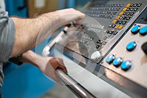 Worker pressing buttons on CNC machine control board in factory.