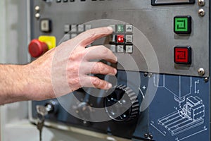 Worker pressing buttons on CNC machine control board in factory.