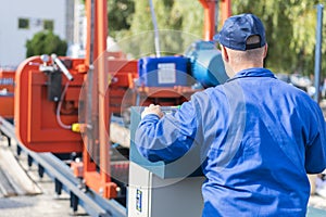 Worker pressing buttons on CNC machine control board in factory. Worker works at a woodworking enterprise