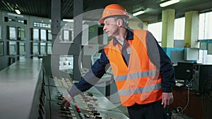 Worker pressing buttons on CNC machine control board in factory. Young engineer