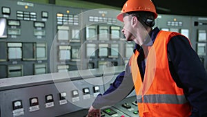 Worker pressing buttons on CNC machine control board in factory. Young engineer