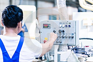 Worker pressing buttons on CNC machine in factory