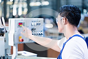 Worker pressing buttons on CNC machine in factory