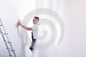 Worker priming white wall next to ladder during home renovation