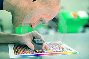 Worker in a printing and press center uses a magnifying glass to check the print quality. Scene showing the print quality control.