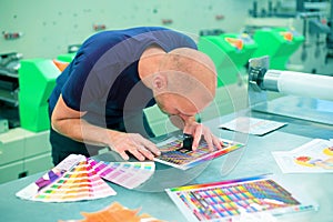 Worker in a printing and press center uses a magnifying glass to check the print quality. Scene showing the print quality control.