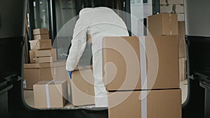 Worker in protective clothing loads boxes of medicines into the trunk of the car