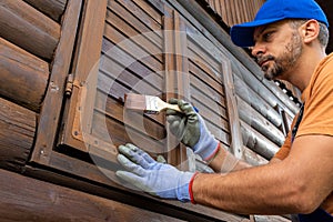 Worker in protective clothing staining wooden window shutters on house external walls