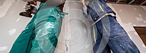 Worker with protective gloves is holdind a perforator with some drywall screws in apartment that is under construction