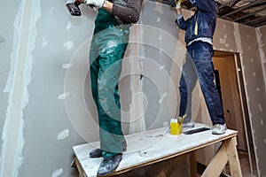 Worker with protective gloves is holdind a perforator with some drywall screws in apartment that is under construction