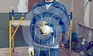 Worker with protective gloves is holdind a perforator with some drywall screws in apartment that is under construction