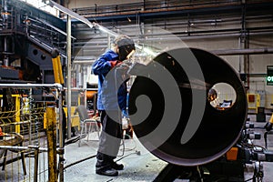 Worker in protective mask grinding pipe after welding