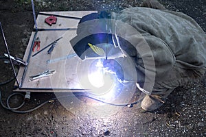 Worker with protective mask weld metal in industrial environment and sparks spread.