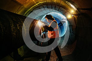 Worker in protective mask welding pipe in tunnel photo