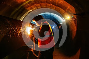 Worker in protective mask welding pipe in tunnel