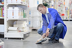 Worker in protective overalls cleaning floor in store