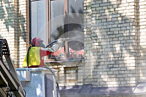 A worker in a protective space suit cleans the facade of an old brick house using an industrial sandblaster