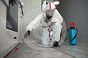 Worker in a protective suit cleans the shelves in the kitchen from cockroaches and ants with a spray, the sanitary service