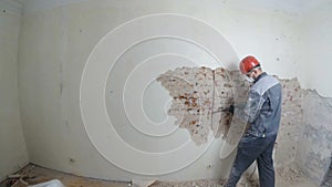 Worker in protective suit demolishes plaster wall. Dirty, hard work. Personal protective equipment. Helmet, respirator