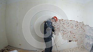 Worker in protective suit demolishes plaster wall. Dirty, hard work. Personal protective equipment. Helmet, respirator