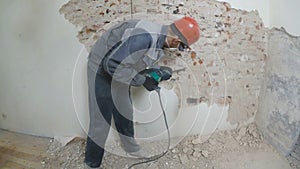 Worker in protective suit demolishes plaster wall. Dirty, hard work. Personal protective equipment. Helmet, respirator