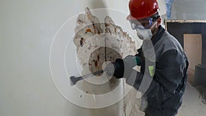 Worker in protective suit demolishes plaster wall. Dirty, hard work. Personal protective equipment. Helmet, respirator