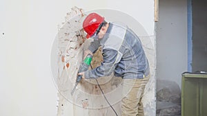 Worker in protective suit demolishes plaster wall. Dirty, hard work. Personal protective equipment. Helmet, respirator