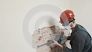 Worker in protective suit demolishes plaster wall. Dirty, hard work. Personal protective equipment. Helmet, respirator