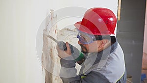 Worker in protective suit demolishes plaster wall. Dirty, hard work. Personal protective equipment. Helmet, respirator