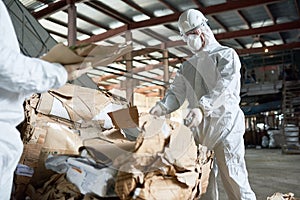 Worker in Protective Suit Sorting Cardboard at Factory