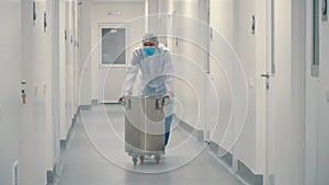 Worker in protective uniform pushing the barrel through corridor in laboratory