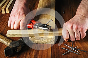 The worker pulls the bent nail out of the board with pliers. Woodworker hands closeup. Working environment in the workshop