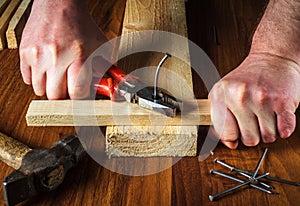 Worker pulls the bent nail out of the board with pliers. Woodworker hands closeup. Working environment in the workshop