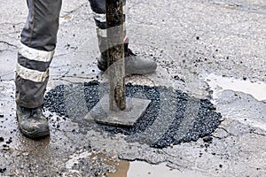 Worker pushing bitumen asphalt in the hole. road repair and maintenance