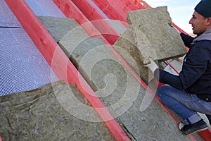 The worker puts mineral wool on the roof, insulating the house