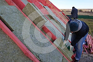 The worker puts mineral wool on the roof, insulating the house