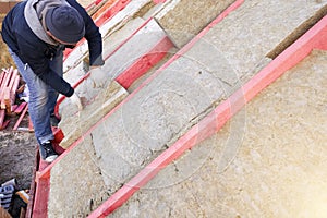 The worker puts mineral wool on the roof, insulating the house