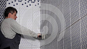 Worker putting fugue on wall tiles joints in bathroom. Man grouting tiles