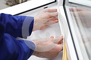 Worker putting rubber draught strip onto window indoors, closeup photo