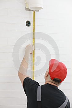 Worker in red cap and work suit with the measuring tape in the kitchen. Man measures the distance, tiler laying a white tile.