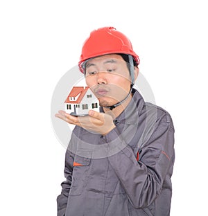 Worker in red hard hat kisses small house model in hand