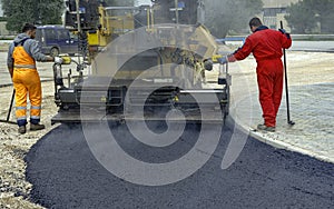 Worker regulate tracked paver laying asphalt