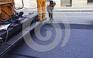 Worker regulate tracked paver laying asphalt