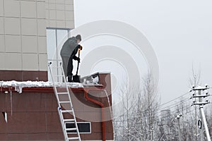 A worker removes snow and ice from the roof cleaning the roof not complying with labor protection rules photo