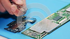 Worker removing broken item from circuit board with tweezers. Hands closeup.