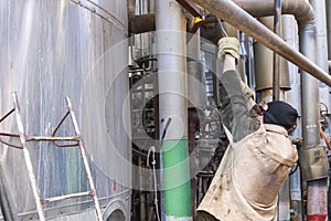 Worker repairman fitter welders in a mask repairing a pipeline, brewing a pipe, repairing equipment at an oil refining