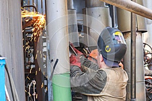 Worker repairman fitter welders in a mask repairing a pipeline, brewing a pipe, repairing equipment at an oil refining