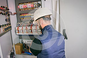 Worker repairs high-voltage equipment. An electrician in a helmet connects the wires of the circuit breakers in the electrical box