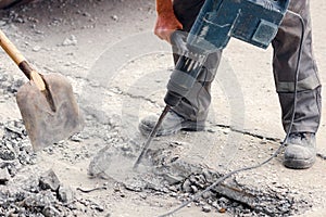 A worker repairs the road surface with a jackhammer on a summer day. Construction works on the road.